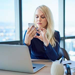blonde woman on her cellphone in front of a laptop